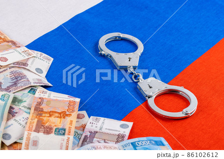 silver colored handcuffs and russian paper rubles currency on russian flag background 86102612