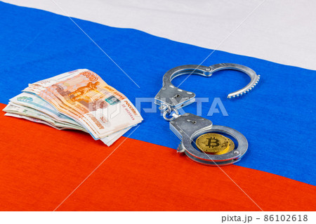 bunch of russian paper rubles currency and bitcoin shiner chained with handcuffs on russian flag background 86102618