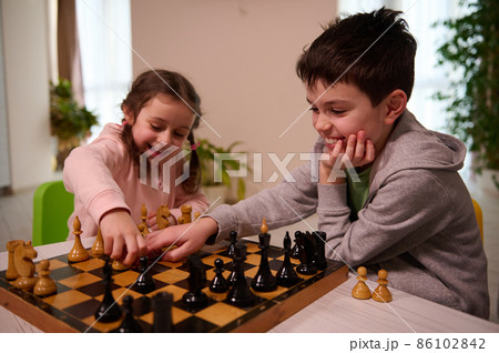 Two adorable kids, boy and girl, brother and sister having great time playing chess game together at home interior. Two adorable kids, boy and girl, brother and sister having great time playing chess game together at home interior. 86102842