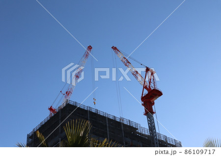 青空と2基のクレーンと建設中のビルと緑の葉に木のある風景 青空と2基のクレーンと建設中のビルと緑の葉に木のある風景 86109717
