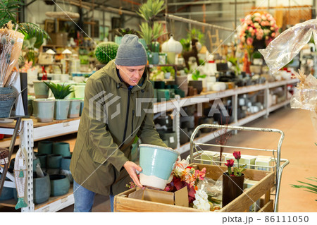 Positive man carefully choosing flower pots in a flower shop Positive man carefully choosing flower pots in a flower shop 86111050