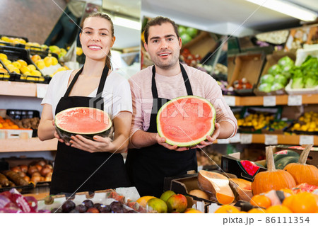 Young saleswoman and salesman holding half of watermelon in hands in fruit store Young saleswoman and salesman holding half of watermelon in hands in fruit store 86111354