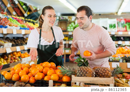 Young woman wearing apron selling fresh oranges to man customer 86112365