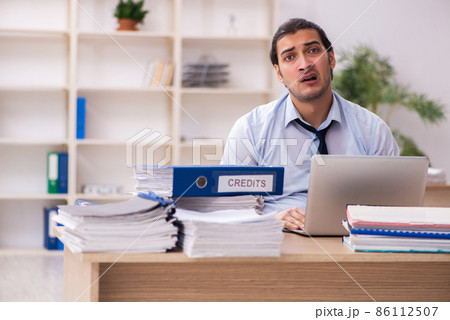 Young male employee and too much work in the office Young male employee and too much work in the office 86112507