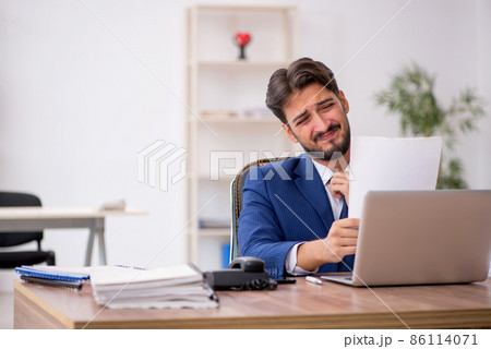 Young male employee unhappy with excessive work in the office Young male employee unhappy with excessive work in the office 86114071