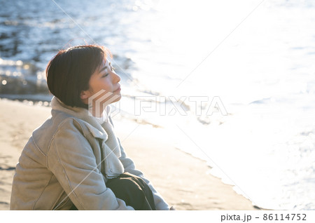 夕日の注ぐ冬の海を見つめる女性 86114752