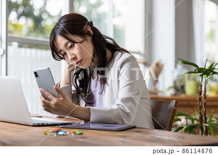 仕事中にスマホを見てネガティブな表情になる女性 86114876