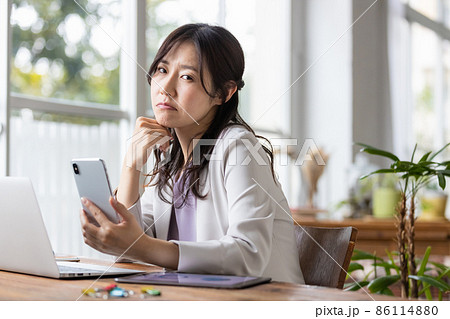 仕事中にスマホを見てネガティブな表情になる女性 仕事中にスマホを見てネガティブな表情になる女性 86114880
