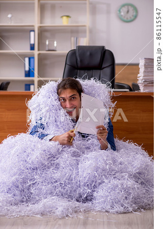 Young male employee and a lot of cut papers in the office Young male employee and a lot of cut papers in the office 86115547