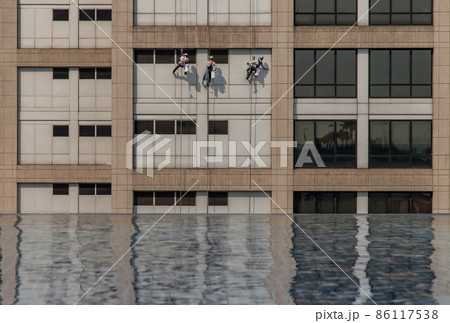 Group of workers cleaning windows service on high rise office building with reflection fiom swimming pool. 86117538