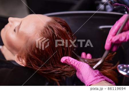 Hairdresser in beauty salon washes his client hair, before procedure of applying natural restoring ingredients and vitamins to hair and haircut. Hairdresser in beauty salon washes his client hair, before procedure of applying natural restoring ingredients and vitamins to hair and haircut. 86119694