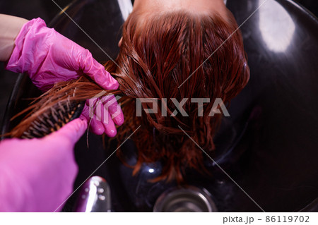 Hairdresser in beauty salon washes his client hair, before procedure of applying natural restoring ingredients and vitamins to hair and haircut. Hairdresser in beauty salon washes his client hair, before procedure of applying natural restoring ingredients and vitamins to hair and haircut. 86119702
