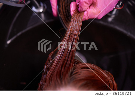 Hairdresser in beauty salon washes his client hair, before procedure of applying natural restoring ingredients and vitamins to hair and haircut. Hairdresser in beauty salon washes his client hair, before procedure of applying natural restoring ingredients and vitamins to hair and haircut. 86119721