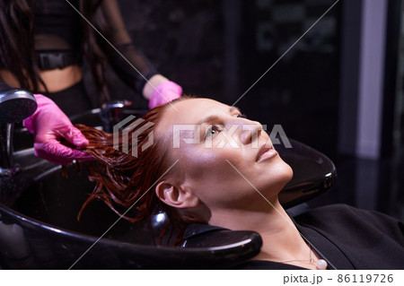 Hairdresser in beauty salon washes his client hair, before procedure of applying natural restoring ingredients and vitamins to hair and haircut. Hairdresser in beauty salon washes his client hair, before procedure of applying natural restoring ingredients and vitamins to hair and haircut. 86119726