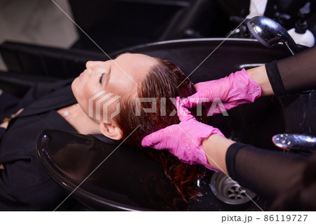 Hairdresser in beauty salon washes his client hair, before procedure of applying natural restoring ingredients and vitamins to hair and haircut. Hairdresser in beauty salon washes his client hair, before procedure of applying natural restoring ingredients and vitamins to hair and haircut. 86119727