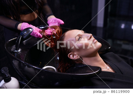 Hairdresser in beauty salon washes his client hair, before procedure of applying natural restoring ingredients and vitamins to hair and haircut. Hairdresser in beauty salon washes his client hair, before procedure of applying natural restoring ingredients and vitamins to hair and haircut. 86119900