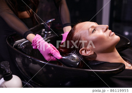 Hairdresser in beauty salon washes his client hair, before procedure of applying natural restoring ingredients and vitamins to hair and haircut. Hairdresser in beauty salon washes his client hair, before procedure of applying natural restoring ingredients and vitamins to hair and haircut. 86119955