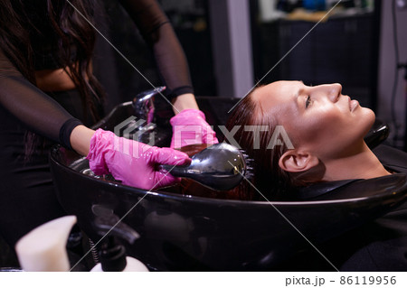 Hairdresser in beauty salon washes his client hair, before procedure of applying natural restoring ingredients and vitamins to hair and haircut. Hairdresser in beauty salon washes his client hair, before procedure of applying natural restoring ingredients and vitamins to hair and haircut. 86119956