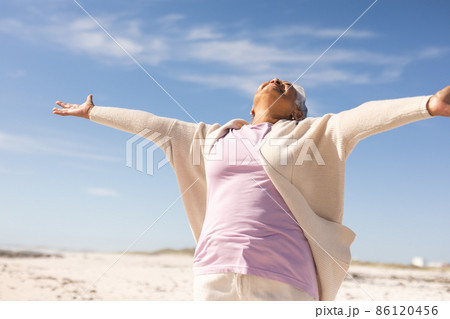 Carefree biracial senior woman with arms outstretched enjoying sunny day at beach against blue sky Carefree biracial senior woman with arms outstretched enjoying sunny day at beach against blue sky 86120456