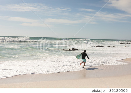 Biracial senior man with surfboard running along shore at beach on sunny day Biracial senior man with surfboard running along shore at beach on sunny day 86120506
