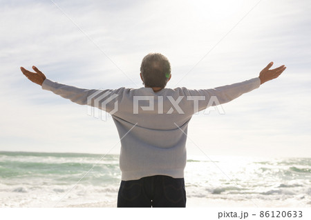 Rear view of biracial senior man with arms outstretched standing at beach during sunny day Rear view of biracial senior man with arms outstretched standing at beach during sunny day 86120633