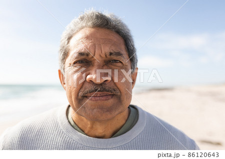 Close-up portrait of biracial senior man with mustache at beach against sky during sunny day 86120643