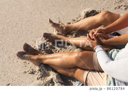 High angle view of romantic senior multiracial couple holding hands sitting on sand at sunny beach High angle view of romantic senior multiracial couple holding hands sitting on sand at sunny beach 86120784