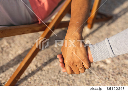 Cropped image of senior multiracial couple holding hands while enjoying retirement at beach 86120843