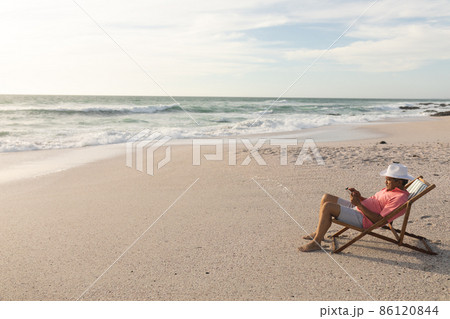 Full length side view of biracial senior man using digital tablet relaxing on folding chair at beach 86120844
