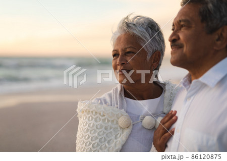 Thoughtful newlywed senior biracial couple looking away while standing at beach during sunset Thoughtful newlywed senior biracial couple looking away while standing at beach during sunset 86120875