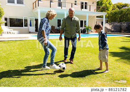 Caucasian grandparents and grandson playing football together in the garden 86121782