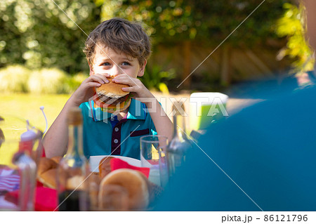 Caucasian boy eating burger sitting together with family at table in the garden 86121796
