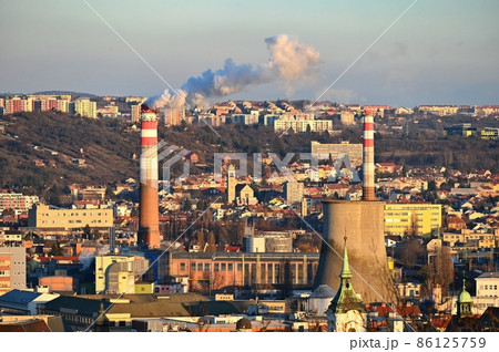 Steaming chimneys with houses in the city. Concept for environment and industry. Background with city landscape at sunset. Brno - Czech Republic - Europe. 86125759