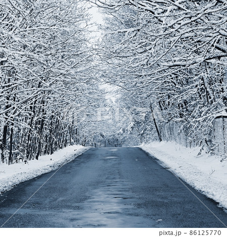 Broken, repaired poor quality asphalt road in winter with snow and icicles. Concept for transport and travel in bad winter weather. Broken, repaired poor quality asphalt road in winter with snow and icicles. Concept for transport and travel in bad winter weather. 86125770
