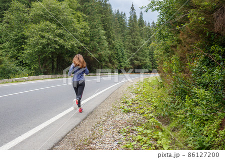 Runner woman running on the mountain road through the forest. 86127200