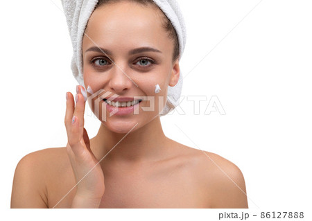 young woman after a shower applies cream on her face 86127888