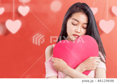 Asian woman holding a red heart with a sad expression 86129696