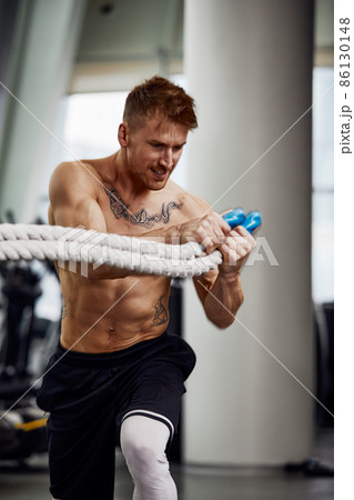 Front view of Attractive young fit and toned sportswoman working out with battle ropes. Motion blur Front view of Attractive young fit and toned sportswoman working out with battle ropes. Motion blur 86130148