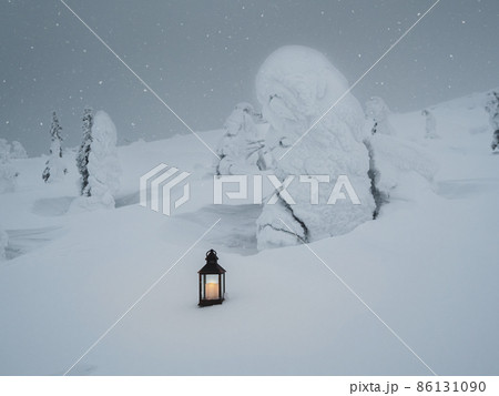 An old lantern with a candle stands on the evening snow in a frosty winter forest with bizarrely twisted trees An old lantern with a candle stands on the evening snow in a frosty winter forest with bizarrely twisted trees 86131090