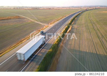 Aerial view of blurred fast moving semi-truck with cargo trailer driving on highway hauling goods in evening. Delivery transportation and logistics concept Aerial view of blurred fast moving semi-truck with cargo trailer driving on highway hauling goods in evening. Delivery transportation and logistics concept 86134210