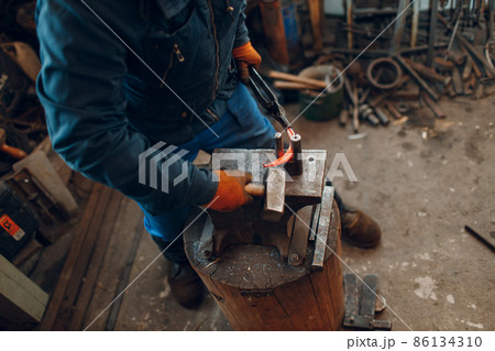 Blacksmith forges and makes metal horseshoe with hammer and anvil at forge. 86134310