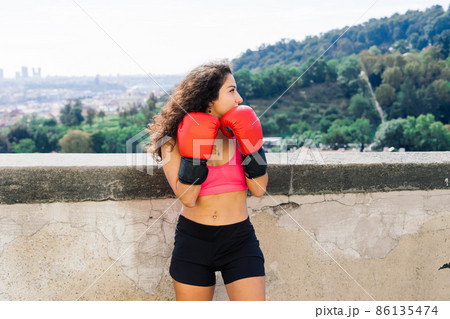 A woman boxer training outdoor - city and nature in background A woman boxer training outdoor - city and nature in background 86135474