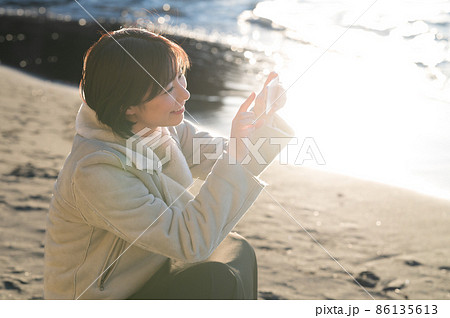 夕日の注ぐ冬の海でスマホを操作する女性 夕日の注ぐ冬の海でスマホを操作する女性 86135613