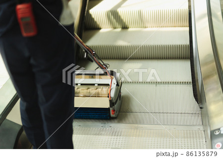 Male cleaner cleaning escalator with mechine in modern building. 86135879
