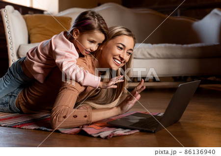 Smiling mom and girl using laptop waving hand Smiling mom and girl using laptop waving hand 86136940