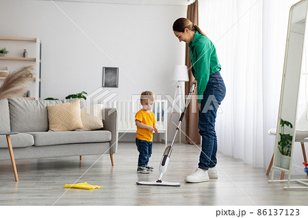 Young mother teaching toddler son cleaning at home, mopping the floor in living room interior, free space Young mother teaching toddler son cleaning at home, mopping the floor in living room interior, free space 86137123