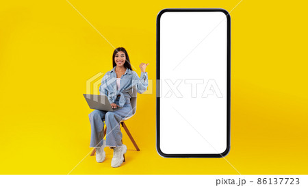 Happy lady using pc pointing at mobile phone screen 86137723