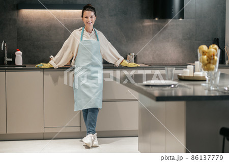 Young woman in apron and gloves in the kitchen Young woman in apron and gloves in the kitchen 86137779