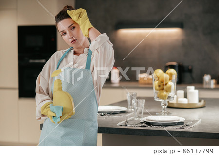Young housewife standing in the kitchen and looking tired after cleaning 86137799