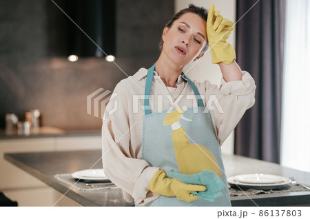 Young housewife standing in the kitchen and looking tired after cleaning Young housewife standing in the kitchen and looking tired after cleaning 86137803